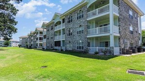 Un immeuble à plusieurs étages, doté d’une façade en pierre, de balcons et d’une pelouse bien entretenue.