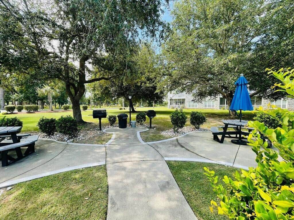 A park with picnic tables, a blue umbrella, and a building in the background.