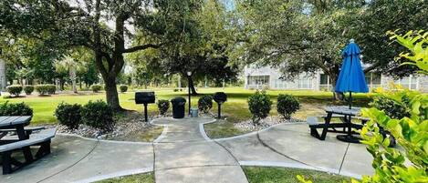 A park with picnic tables, a blue umbrella, and a building in the background.