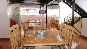 Un restaurante con mesas y sillas de madera, una pantalla de televisión y una escalera.