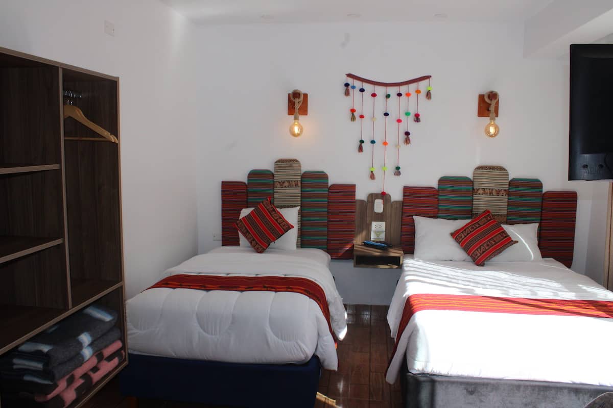 A hotel room with two beds, a wardrobe, and a wall-mounted TV.