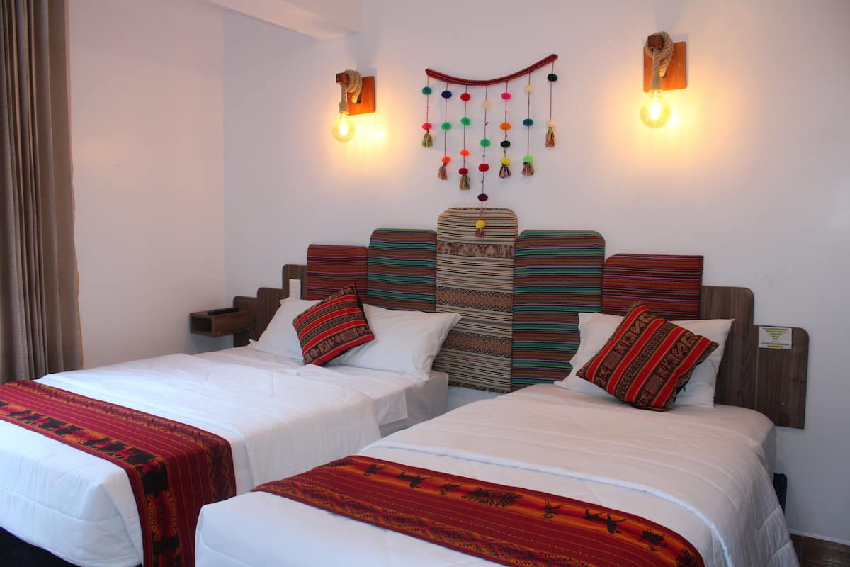 A hotel room with two beds, a decorative wall hanging, and two wall-mounted lights.