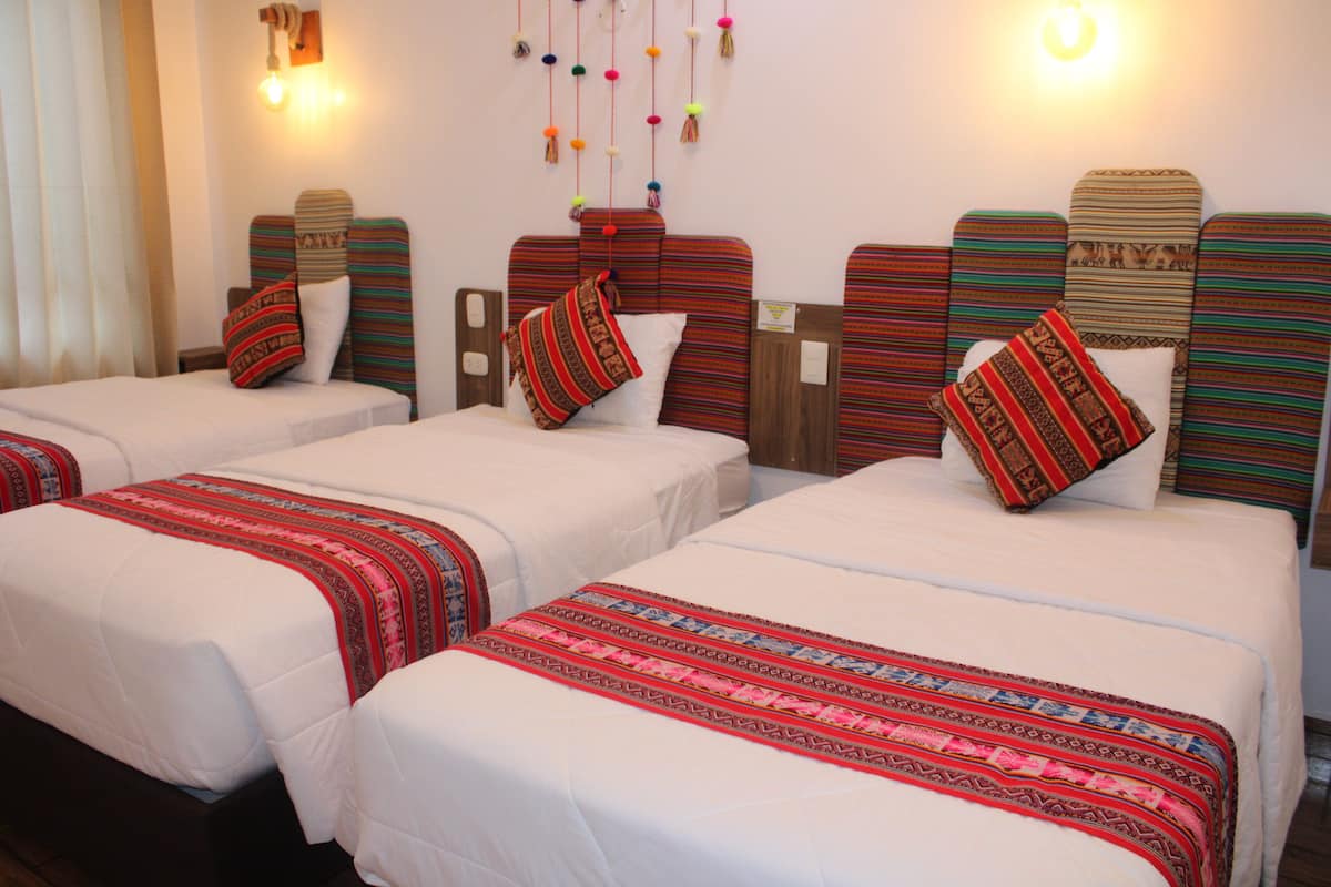 A hotel room with three single beds, each with a striped headboard and a patterned bedspread.