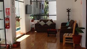 Amplia sala de estar con piso de madera, un sofá marrón, una mesa de centro roja y plantas en macetas.