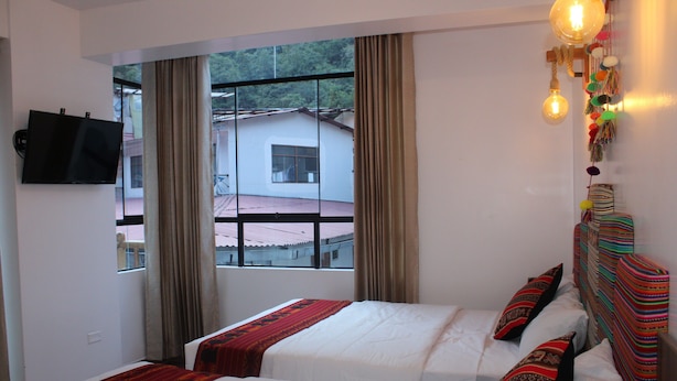 Habitación de hotel con dos camas, televisor y ventana con cortinas.