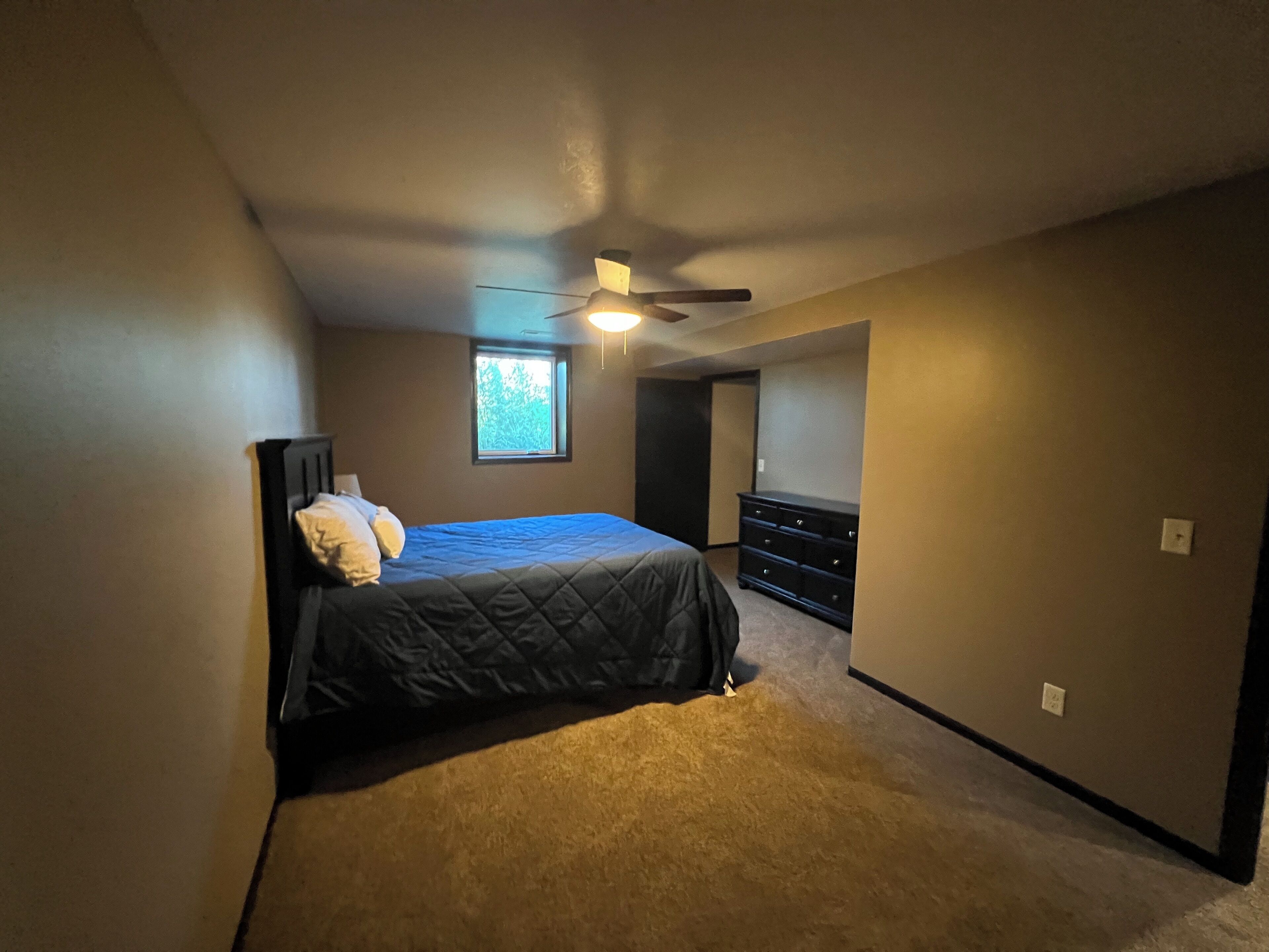 A bedroom with a bed, dresser, ceiling fan, and a window.