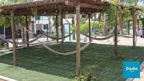 A wooden pergola with vines, surrounded by green grass and palm trees. - Azul Marino El FARO (Mazatlán)