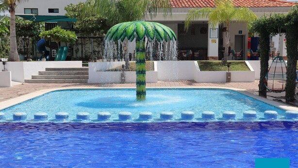 A swimming pool with a central water feature and a palm tree sculpture. - Azul Marino El FARO (Mazatlán)