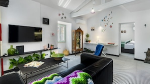 Una sala de estar moderna con un sofá de cuero negro, un televisor de pantalla plana y una mesa de centro. Se observa un mueble de madera con puertas de cristal y una silla azul.