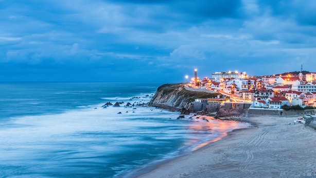 Un pueblo costero con edificios a lo largo del acantilado, un faro y una playa.