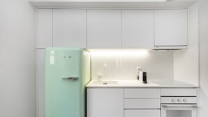 Una cocina compacta con armarios blancos, un refrigerador verde, un lavamanos, una estufa y un horno.