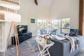 A spacious living room with a large window, a sofa, a TV, and a decorative table.