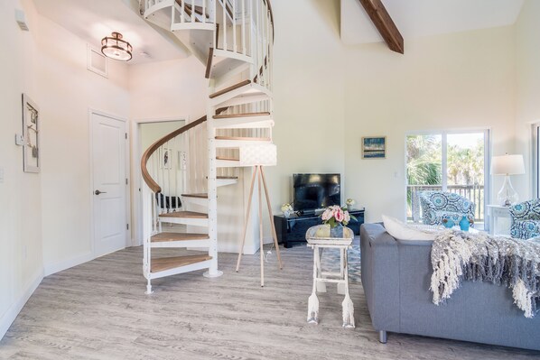 A spacious living area with a spiral staircase, a grey sofa, and a television.