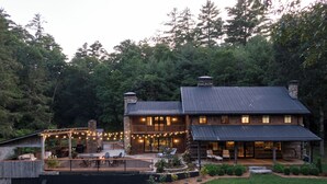 A two-story log cabin with a deck and outdoor seating area, surrounded by a wooded landscape. - The Peregrine: Flat Mountain Farm - expansive luxury home on historic 28 acre rhododendron farm (Highlands)