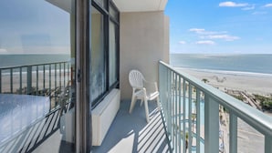 Un balcon avec vue sur la plage, une chaise blanche et un espace piscine.