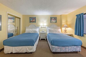 Una camera d'albergo con due letti, un comodino con lampade, uno specchio e due quadri appesi al muro.