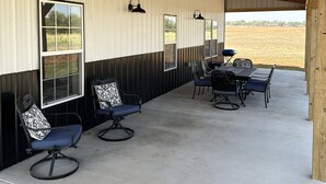 A covered outdoor patio with a concrete floor, metal-framed chairs, and a table. - The Great Plains Escape (Enid)