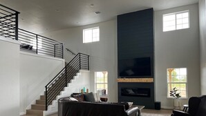 A spacious living room with a staircase, a fireplace, and a large TV. - The Great Plains Escape (Enid)