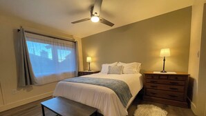 A bedroom with a bed, two bedside tables with lamps, a bench, a fur rug, a ceiling fan, and a window with curtains. - Mountainside ski-in condo near Ski Time Square  (Steamboat Springs)