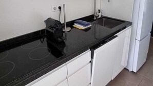 A modern kitchen with white cabinets, a black countertop, a stainless steel range hood, a built-in oven, a sink, and a white refrigerator.