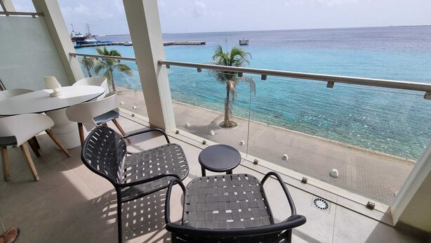 A balcony with a table and chairs, overlooking a beach and the sea.