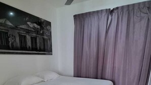 A bedroom with a bed, a ceiling fan, a window with curtains, and a wall-mounted picture.