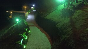 Un sendero nocturno que lleva a un edificio con una escalera y una pequeña construcción a la izquierda.
