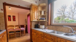 Une cuisine avec des meubles de rangement en bois, un évier à deux bacs et un coin repas comprenant une table et des chaises.