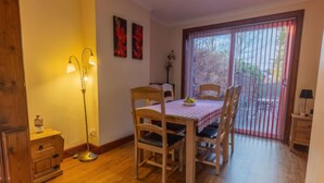 Un coin repas avec une table et des chaises en bois, un lampadaire et une vue à travers une porte-fenêtre coulissante.