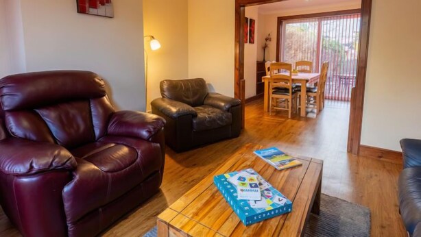 Un salon avec un canapé en cuir rouge, un fauteuil en cuir noir et une table basse en bois sur laquelle se trouve une boîte de Scrabble.