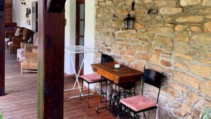 Un espacio de estar al aire libre techado, con pared de piedra, mesa y sillas de madera.