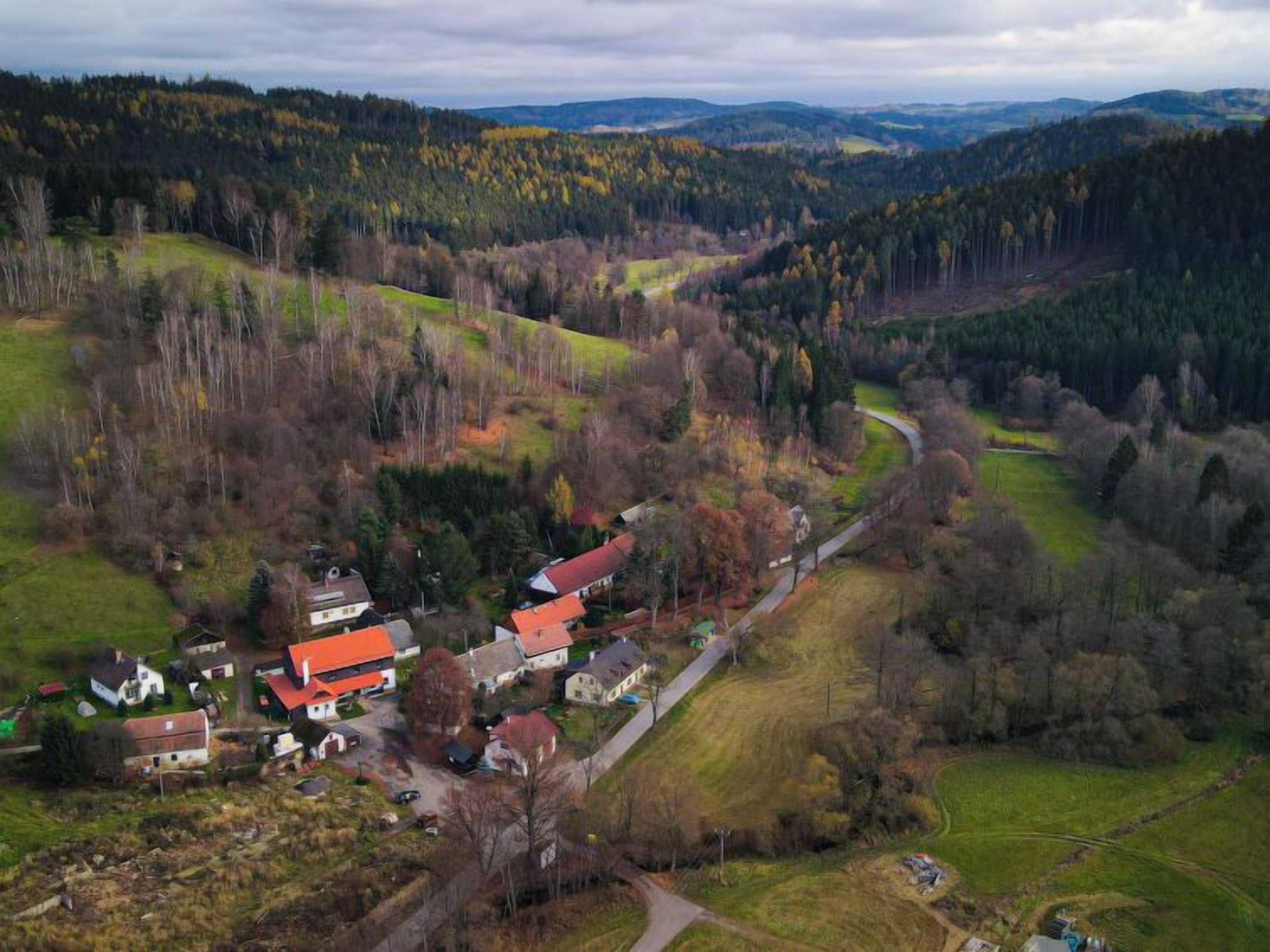 Vue aérienne d’un village rural avec des maisons, une route sinueuse et des collines boisées environnantes.