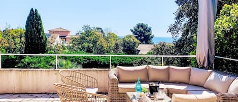 A rooftop terrace with wicker furniture, a sofa, and a table with drinks.