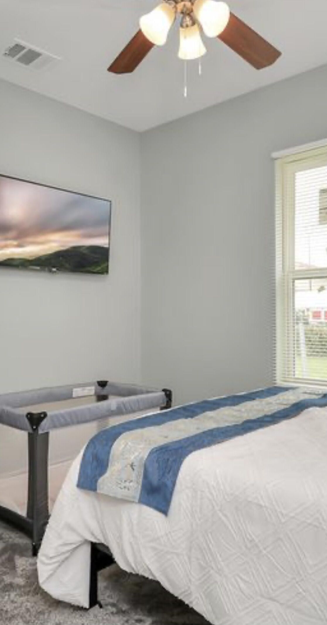 Une chambre à coucher avec un lit, un ventilateur de plafond, une fenêtre avec des stores et un tableau accroché au mur.