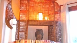 Une pièce avec un ventilateur de plafond, un canapé à motifs, une tapisserie murale tissée et un vase posé sur une table.