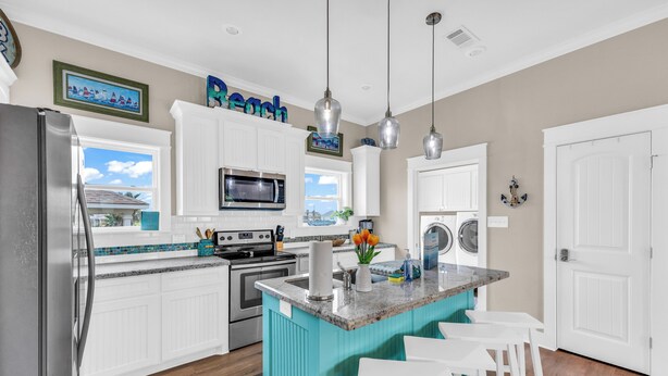 A kitchen with white cabinets, a turquoise island, stainless steel appliances, and a view of the outdoors. - Casa Crystal - Relax and create unforgettable memories (Bolivar Peninsula)