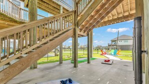 A covered outdoor area with a wooden staircase, a concrete floor, and a view of a residential neighborhood. - Casa Crystal - Relax and create unforgettable memories (Bolivar Peninsula)