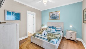 A bedroom with a bed, nightstands, a ceiling fan, and artwork on the walls. - Casa Crystal - Relax and create unforgettable memories (Bolivar Peninsula)