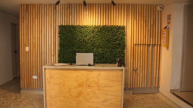 A reception desk with a wooden finish, a green vertical garden, and a fire extinguisher on the wall. - Hotel La Carpita (Medellín)
