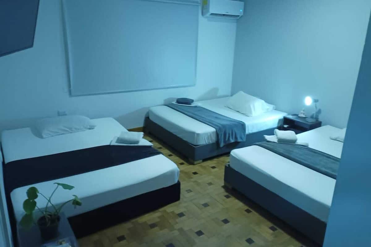 A room with two single beds, a small bedside table with a lamp, and a large window.