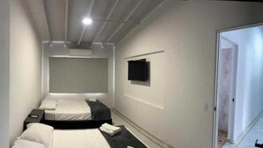 A compact hotel room with two beds, a flat-screen TV mounted on the wall, and a door leading to another room. - Hotel La Carpita (Medellín)