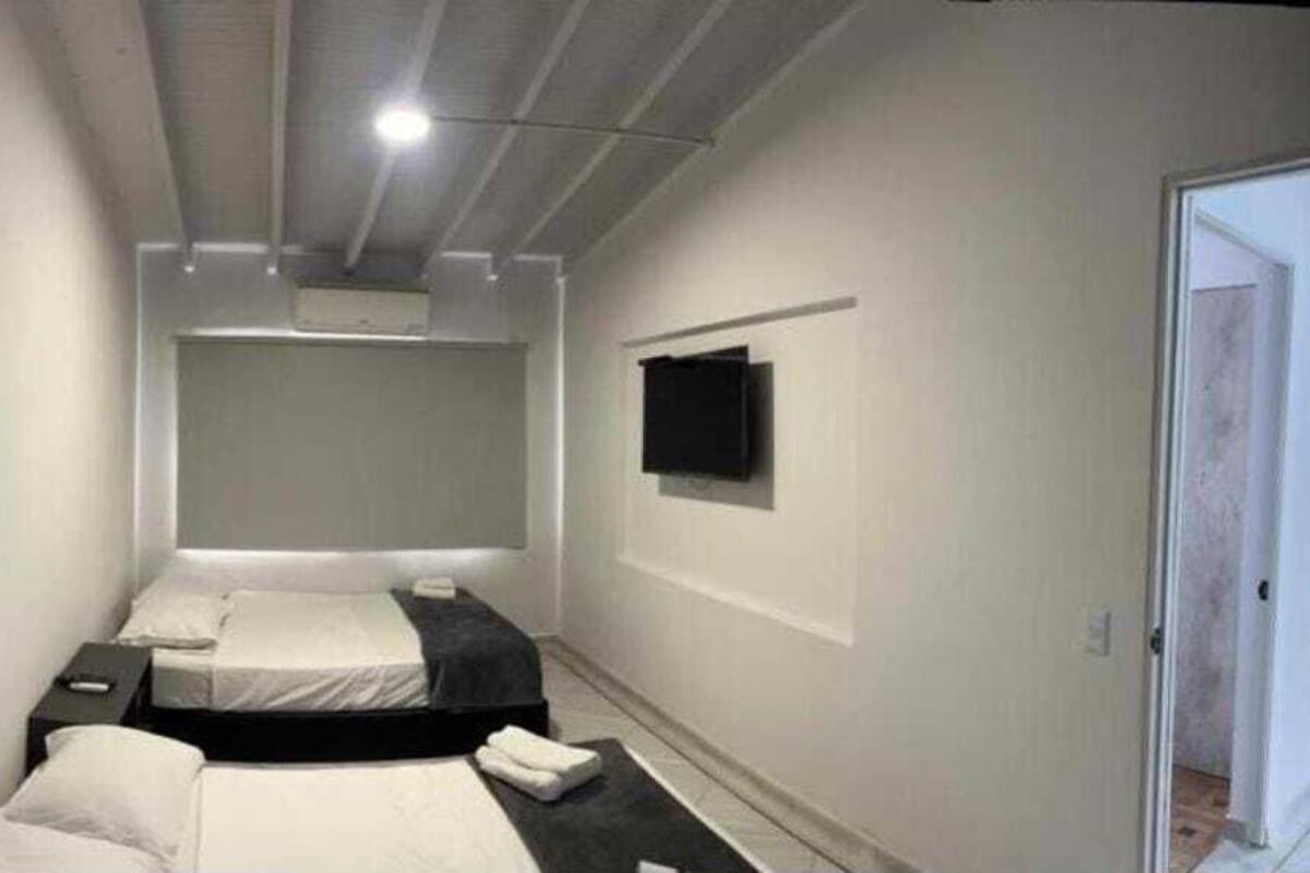 A compact hotel room with two beds, a flat-screen TV mounted on the wall, and a door leading to another room.