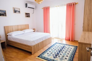 Un dormitorio con cama de madera, un tapete azul estampado, cortinas rosas y cuadros en la pared.