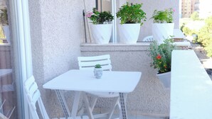 Ein Balkon mit weißem Tisch und Stühlen, Blumentöpfen und einem Fenster.