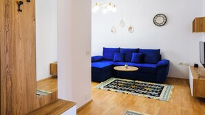 Ein modernes Wohnzimmer mit einem blauen Ecksofa, Holzboden, einer Kristallleuchtreiter und einer Wanduhr.