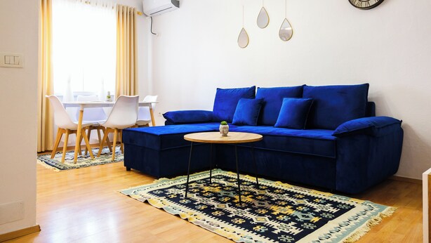 Ein modernes Wohnzimmer mit einem blauen Sofa, einem kleinen runden Tisch und einem gemusterten Teppich.