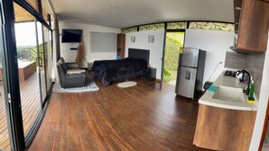 Una habitación moderna con cama, sofá, televisión y una zona de cocina con lavaplatos y refrigerador.