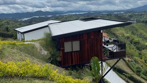 Una casa moderna con techo inclinado, rodeada de exuberante vegetación y una vista panorámica de montañas distantes y un lago.