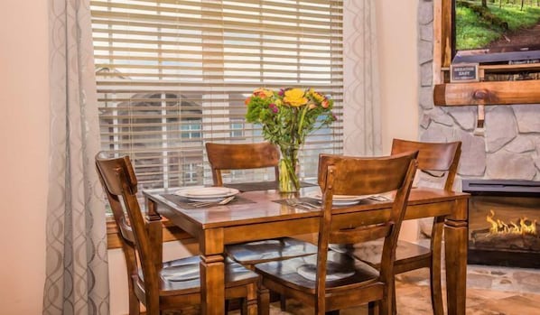 A dining area with a wooden table and chairs, a vase with flowers, and a fireplace.