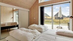 A bedroom with a large bed, a bedside table, a mirror, and a sliding glass door leading to an outdoor area.